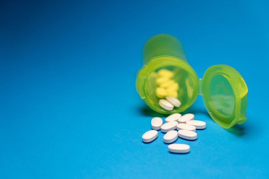 A tablet splitter being used to cut a white pill in half on a wooden table